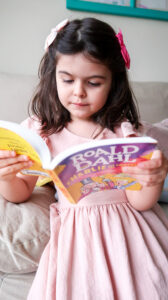 Menina de 4 anos lendo livro Charlie and the Chocolate Factory, do autor Roald Dahl